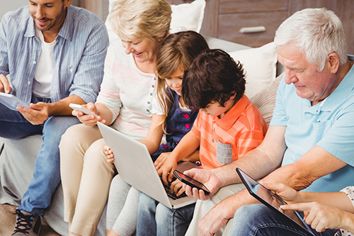 Family with grandparents using technology while sitting on sofa