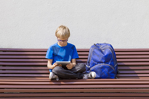 Boy with glasses using tablet PC. Child sitting on the bench. Outdoor. Free copy space. Education, technology, people concept